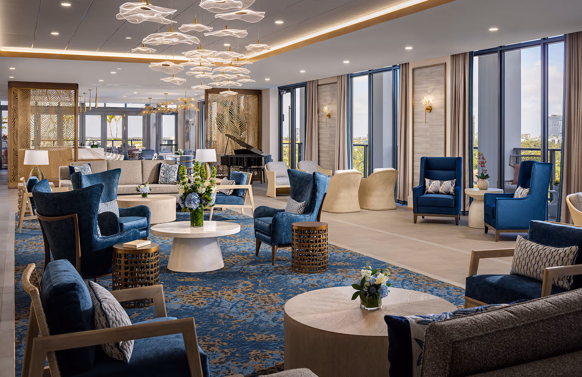 Bright, modern senior living lounge with blue chairs, coffee tables, and large windows.