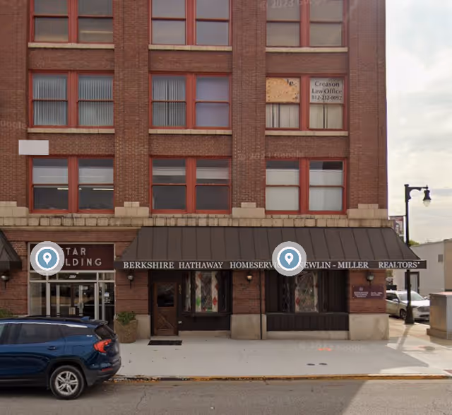 A multi-story brick building with a storefront awning and a parked car on the street.