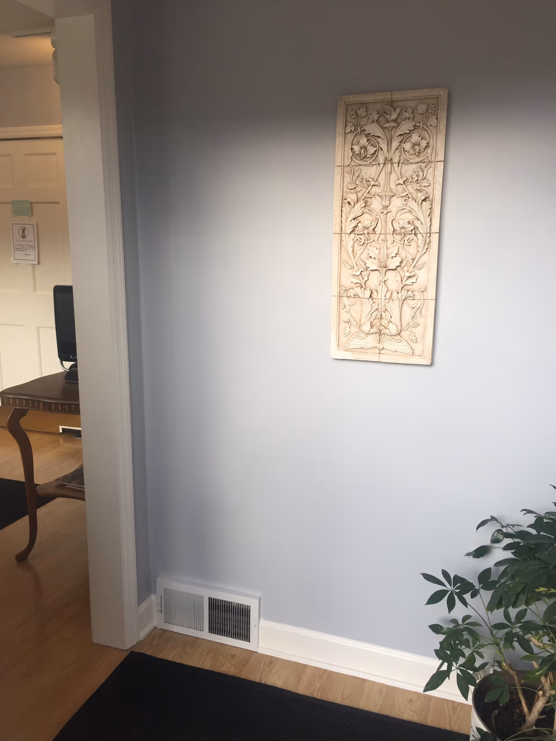 Blue-gray hallway interior with decorative panel, vent, doorway to desk area, and a potted plant