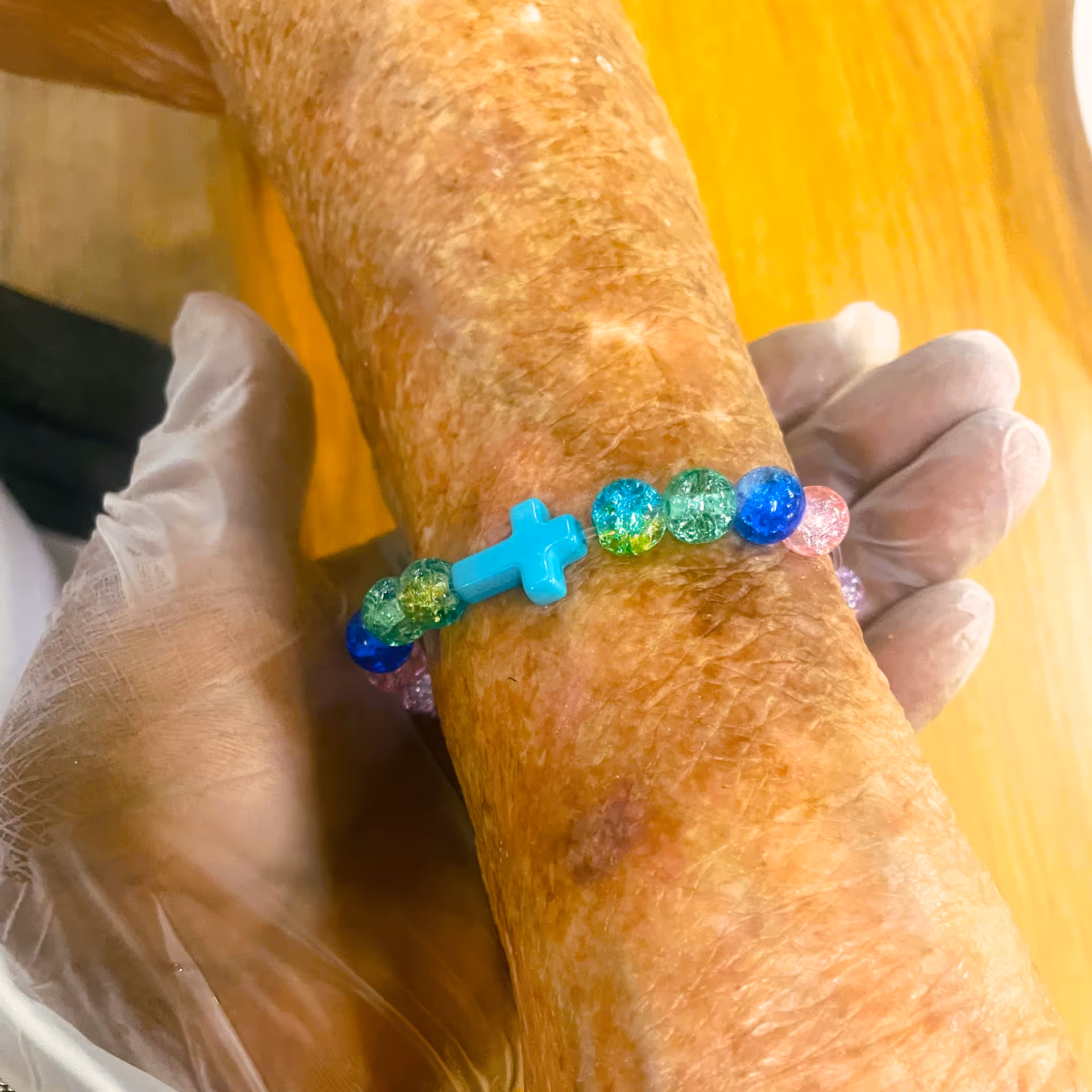 Close-up of an elderly wrist wearing a multicolored bead bracelet with a blue cross.