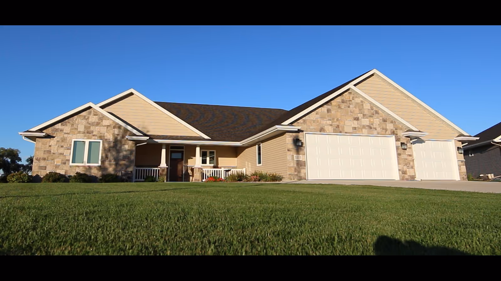 Single-story house with stone and beige siding, a large front lawn, and a two-car garage.