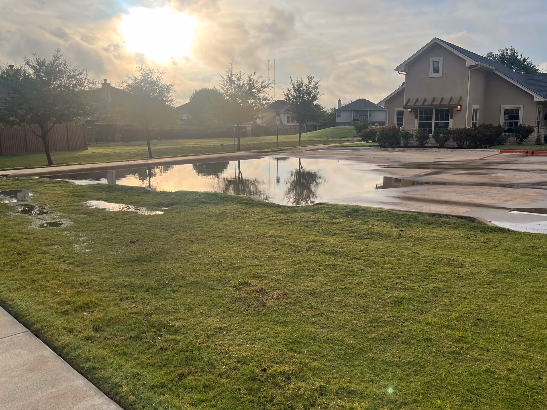 The front exterior of Emerald Cottages of Round Rock shows a large puddle and lawn.