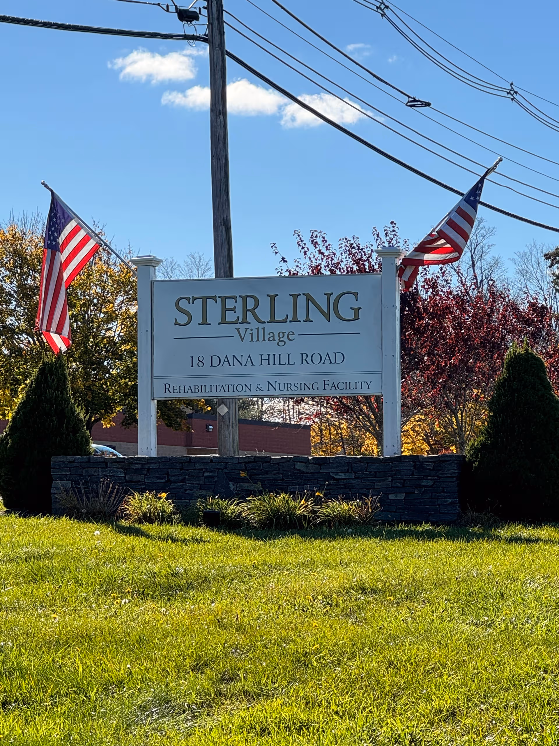 Exterior view of Sterling Village sign with flags and manicured landscaping at the facility entrance.