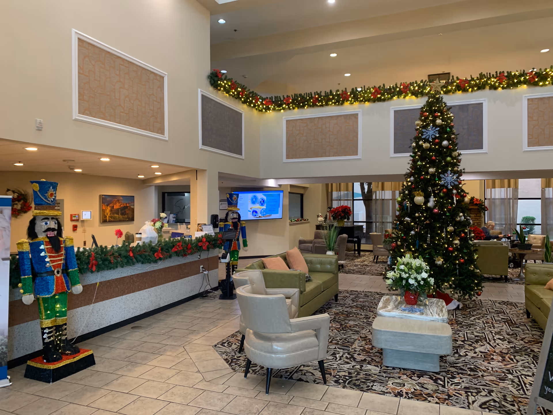 Bright, festive senior living lobby featuring a large Christmas tree, garlands, and nutcracker statues.