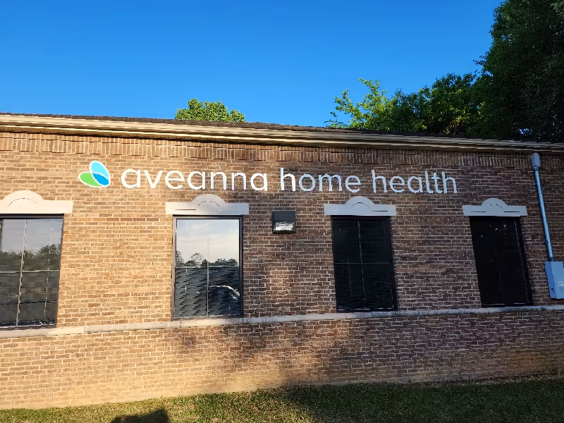 Exterior brick building with Aveanna Home Health sign and several windows under a clear blue sky.