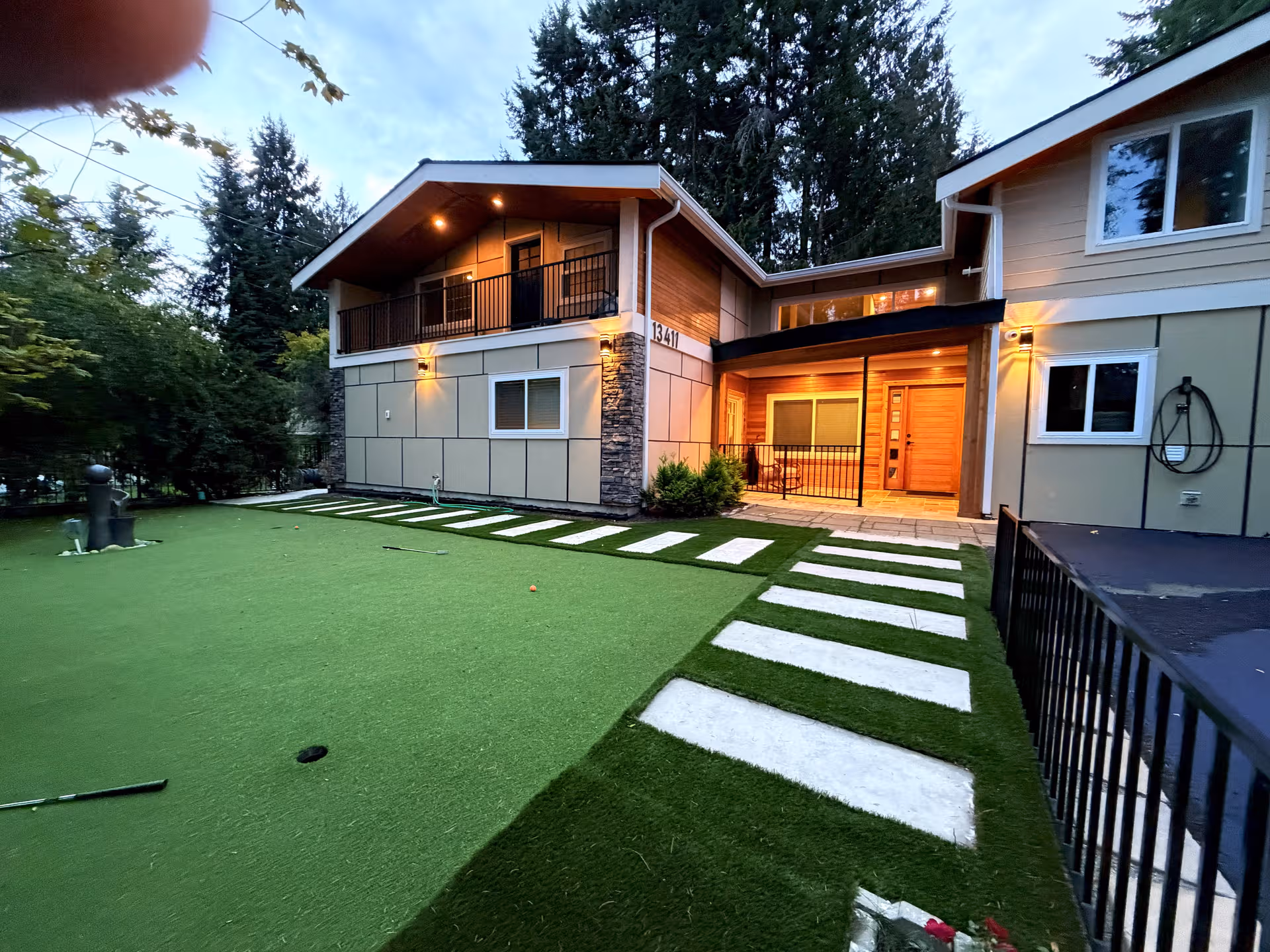 Exterior view of a two-story senior living facility with green artificial lawn and stepping stone path.