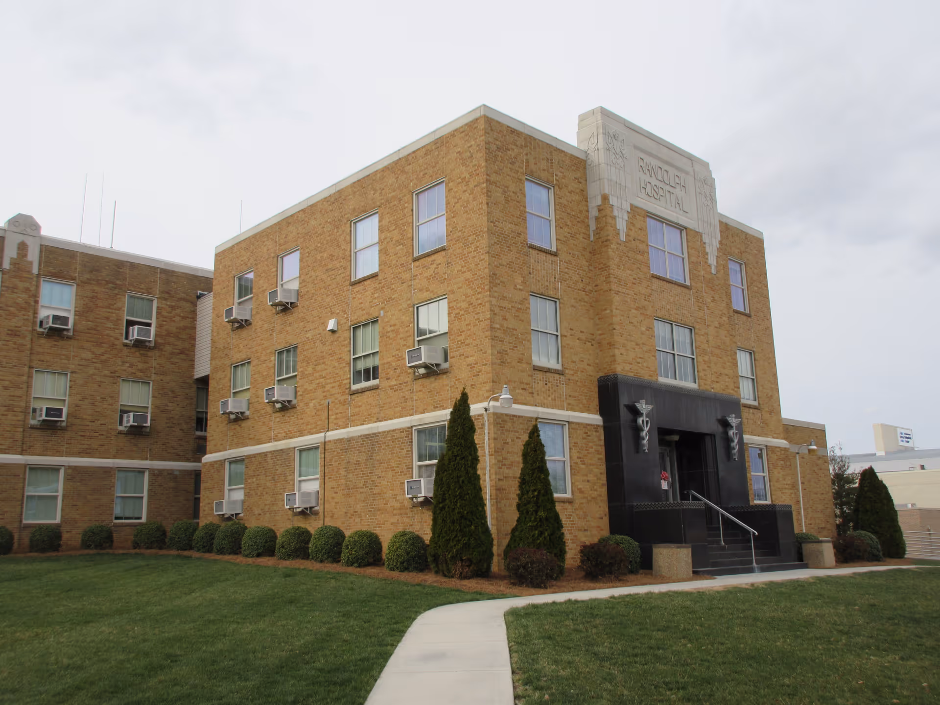 Brick facility named Randolph Health with a front entrance, well-kept lawn, and windows.