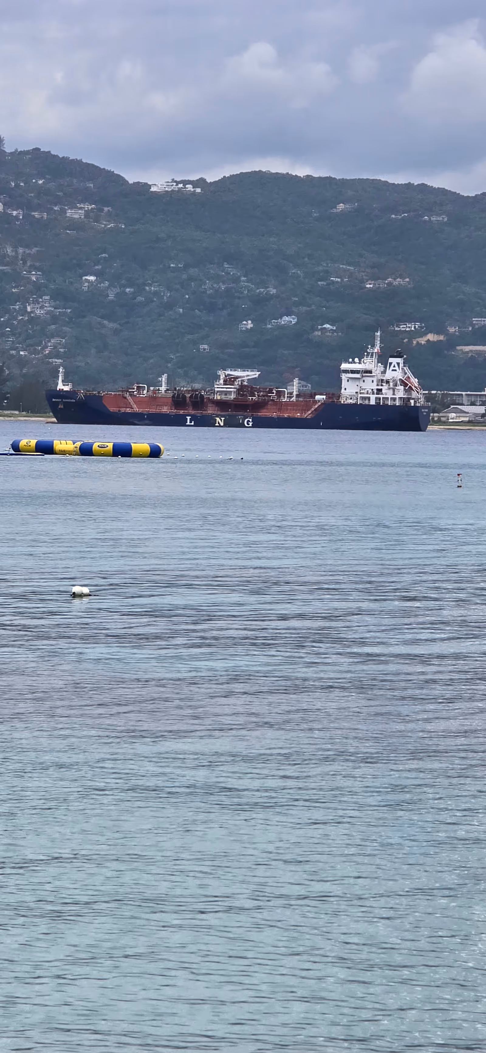 A large cargo ship on calm water with hills in the background.