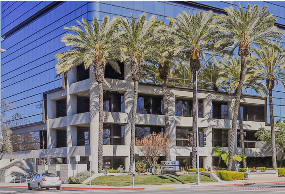 Modern multi-story building facade with palm trees and a street intersection.
