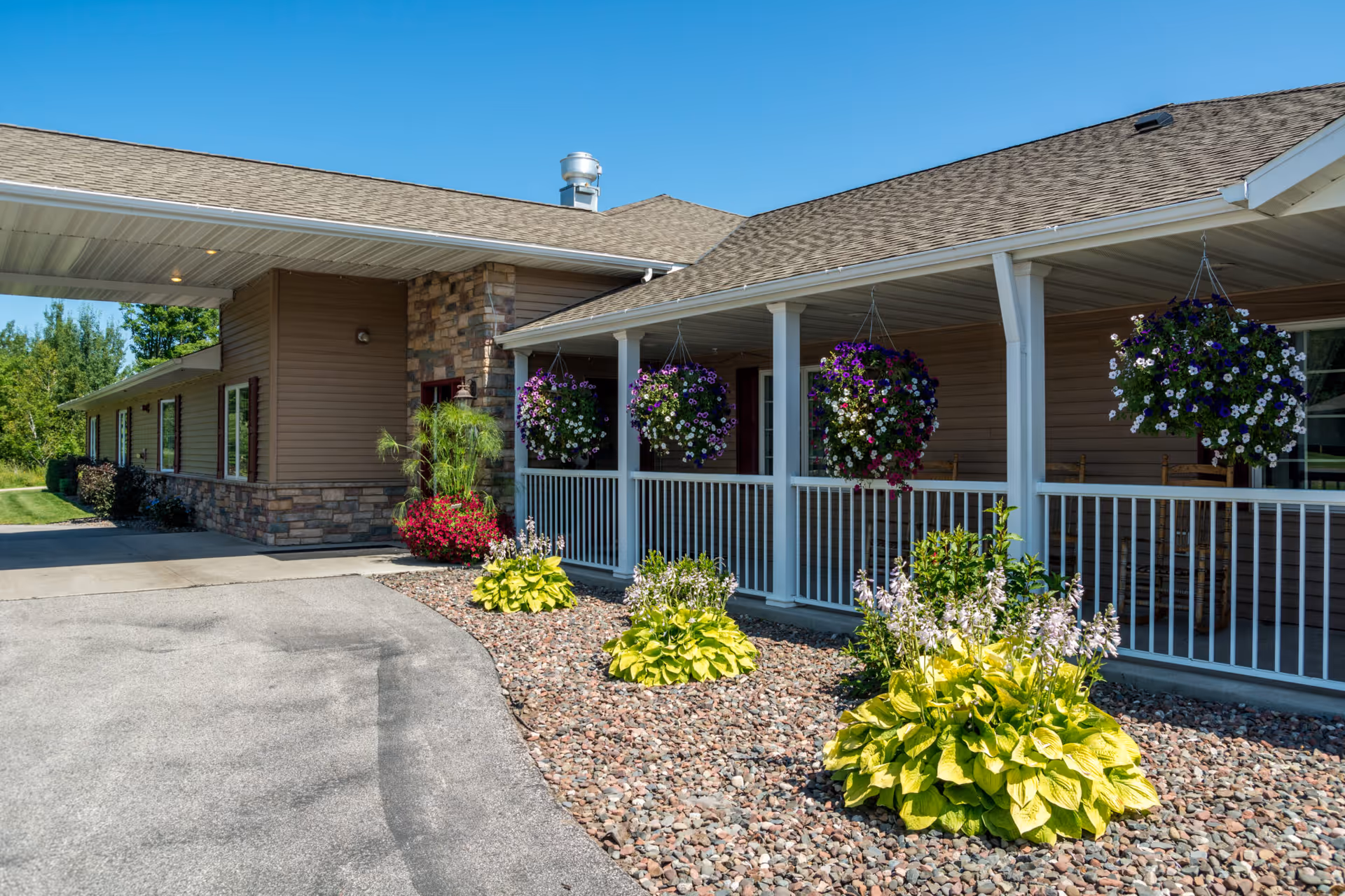 Entrance of a single-story building with a covered porch, hanging flower baskets, and landscaped rock beds.