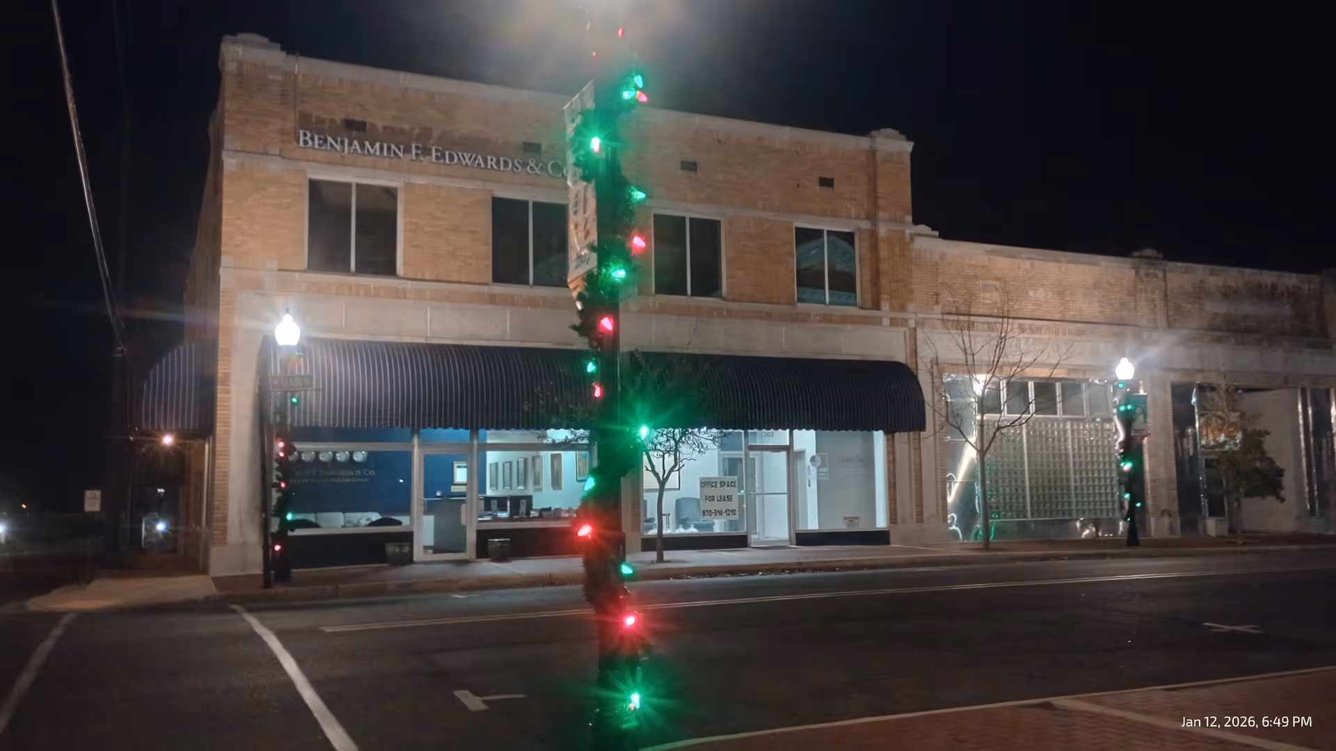 Night exterior of a brick building with a striped awning and lit storefront windows.