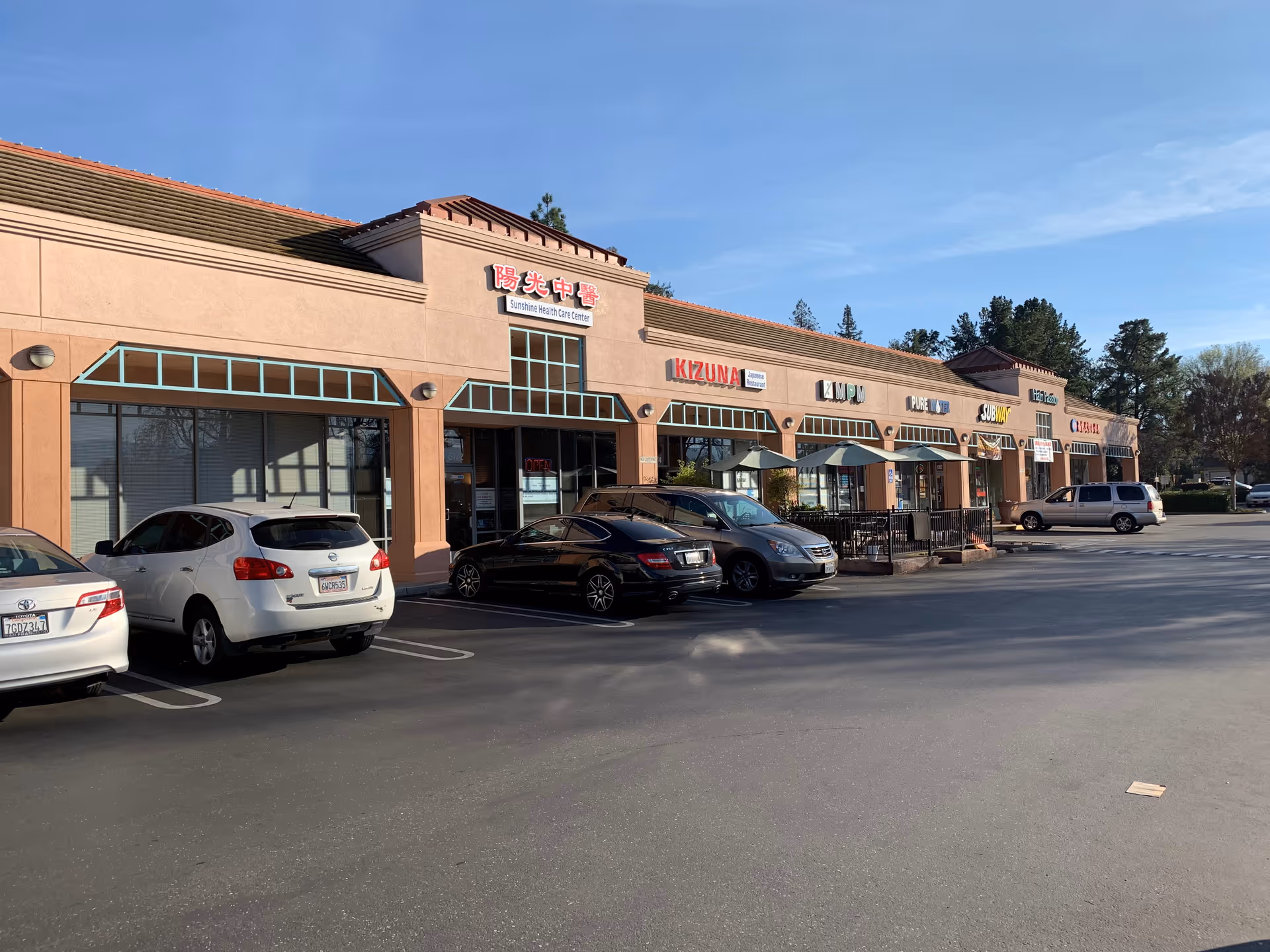 Exterior view of a strip mall with Sunshine Health Care Center sign and parked cars.