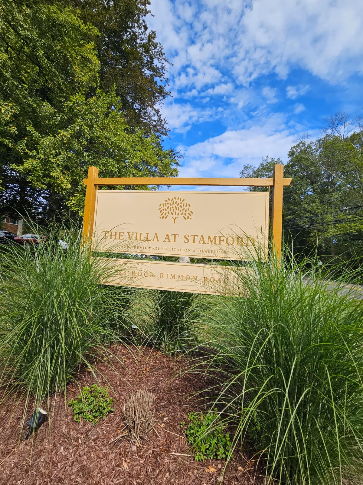 A large beige sign reading The Villa at Stamford amid green landscaping and blue sky.