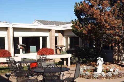 Outdoor patio with metal chairs and table, potted plants, and a small statue near the building