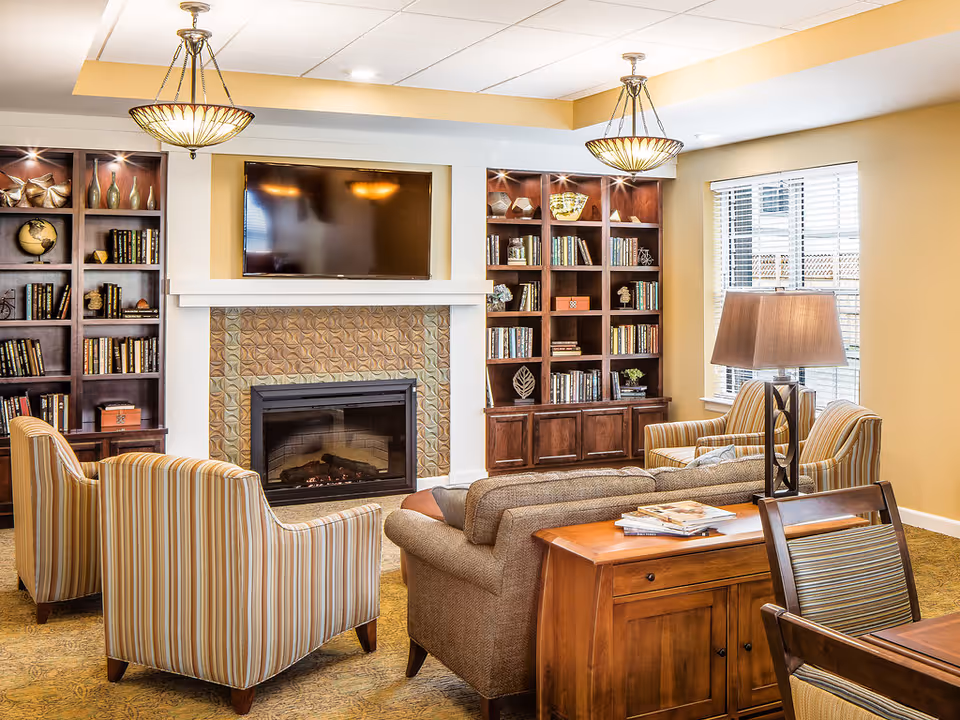 Cozy living room in a senior facility with fireplace, bookshelves, and comfortable seating.