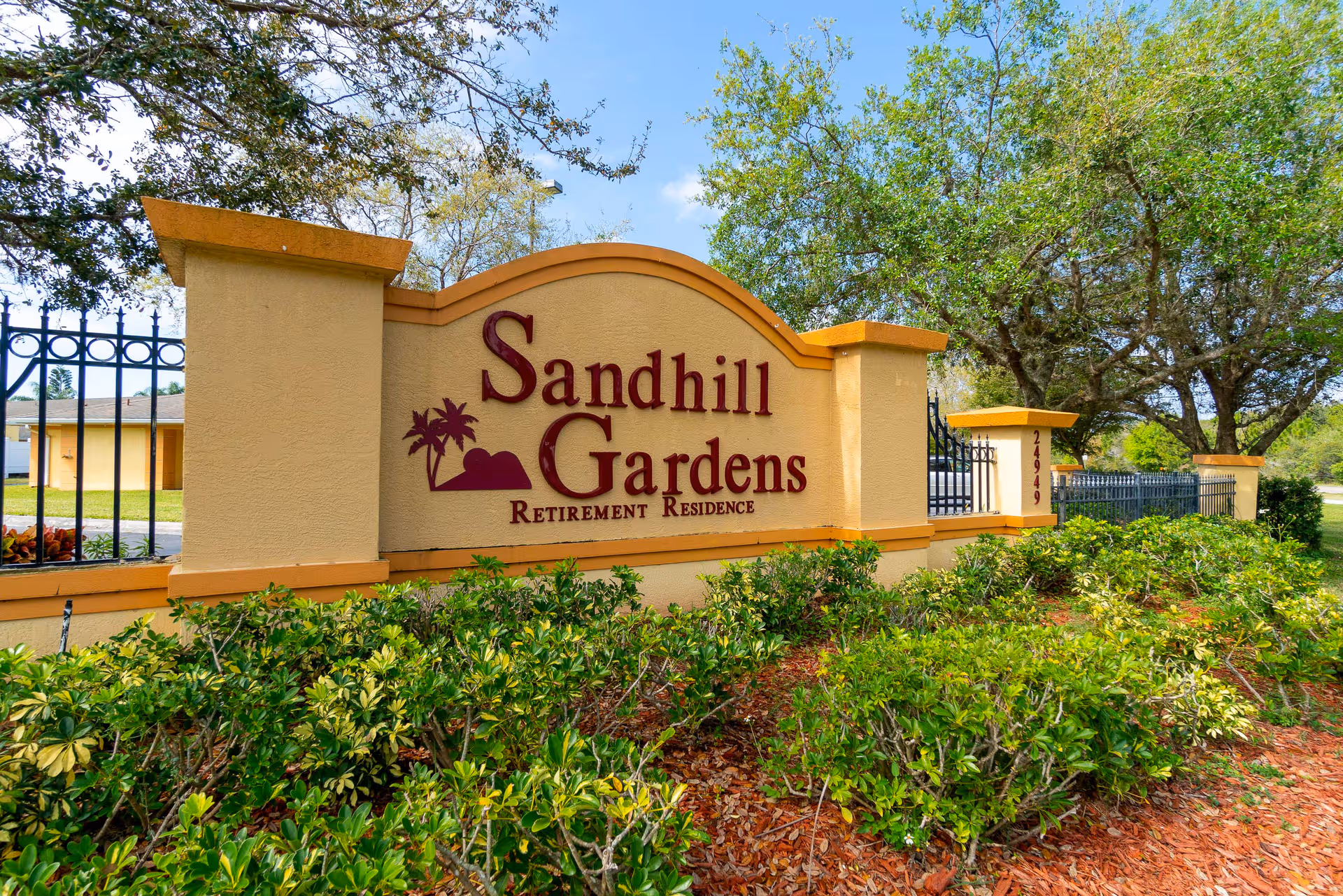 Sandhill Gardens retirement residence entrance sign with landscaping and trees.
