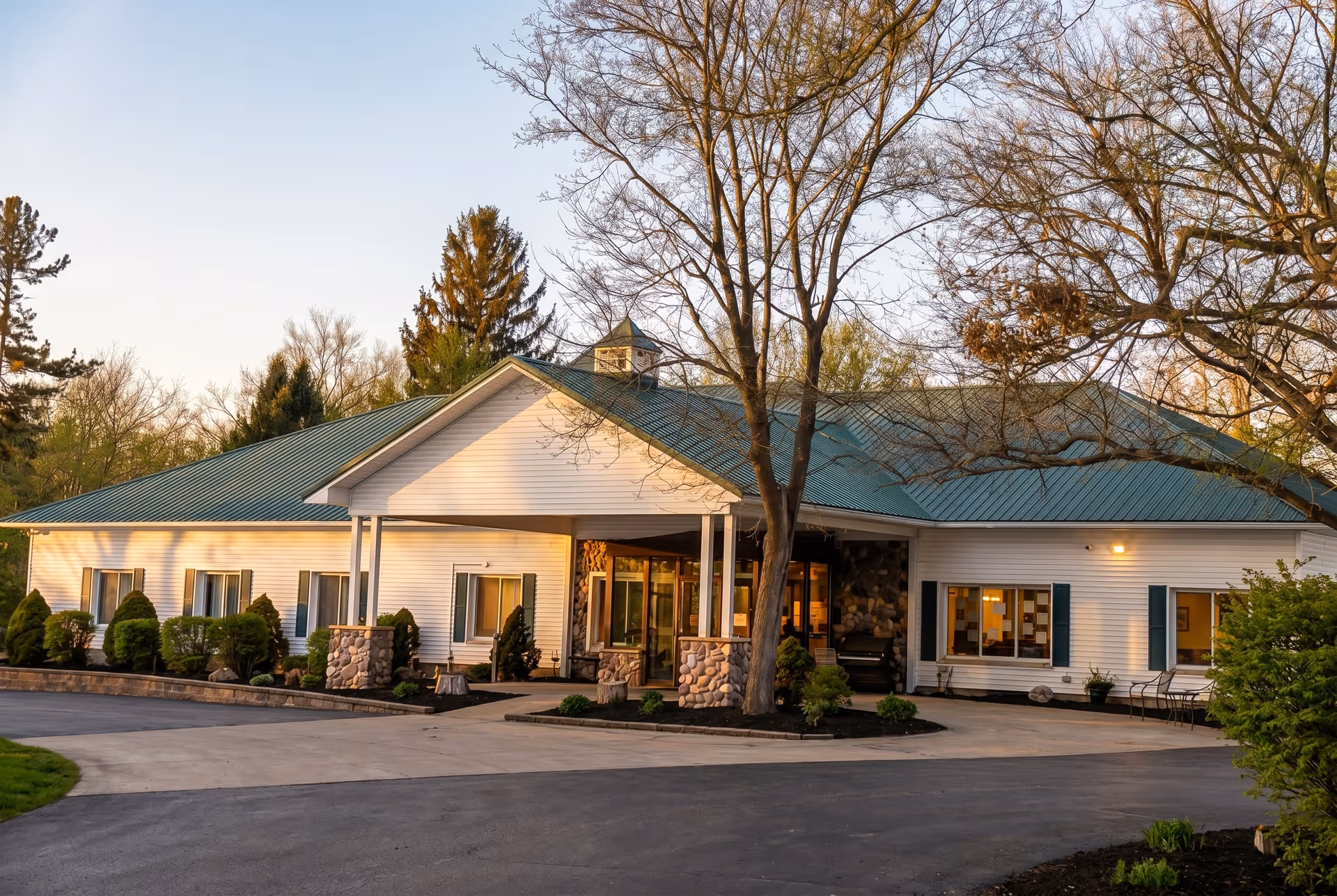 Sunny exterior view of Ridgeway Assisted Living and Memory Care entrance with trees and driveway.