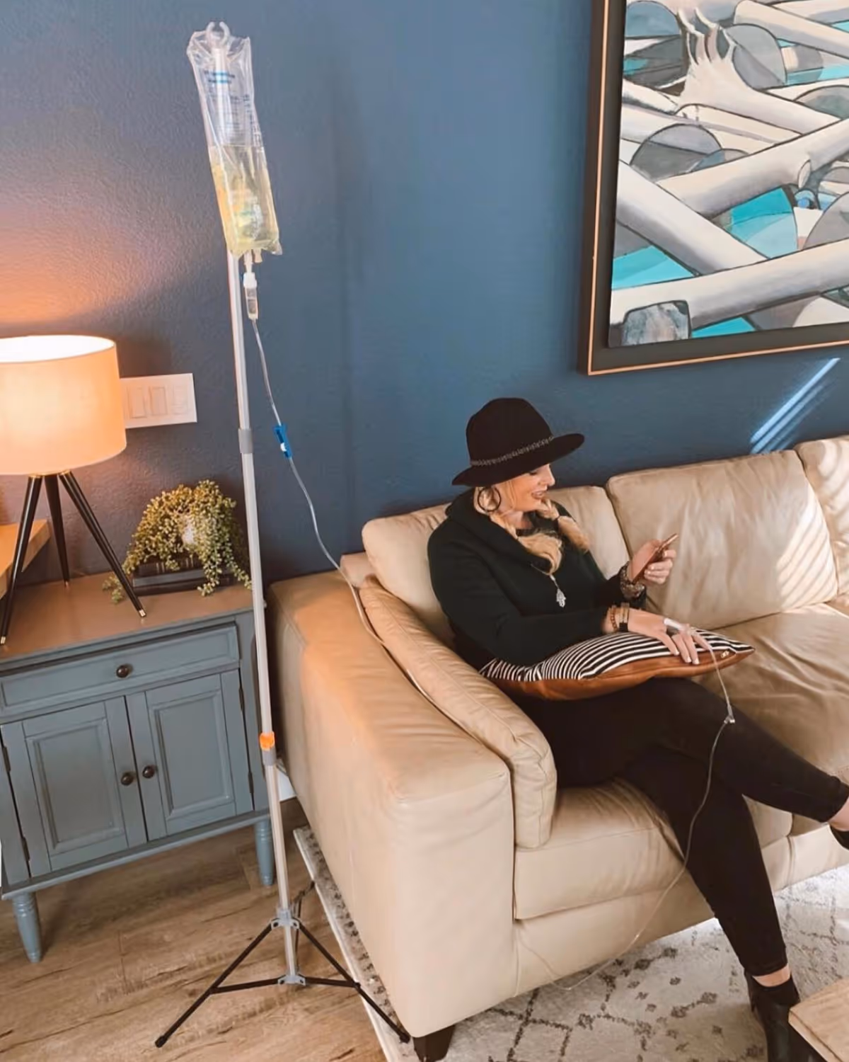Person sits on a cream sofa receiving IV therapy in a stylish living room.