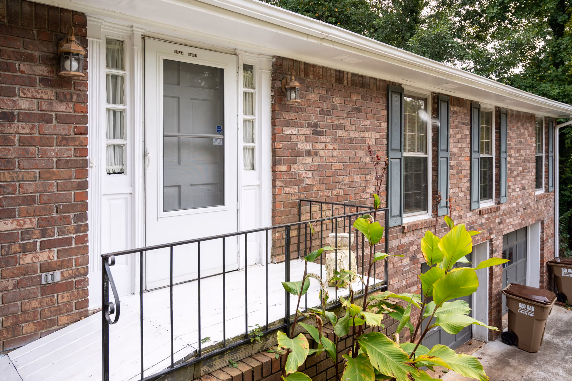 Brick senior care home exterior with a white door and railing by greenery