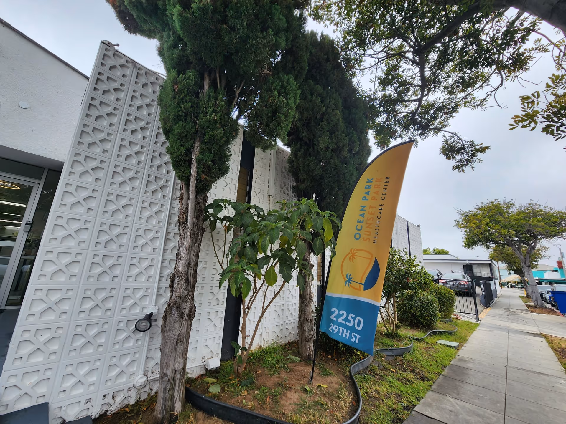 Exterior view of a building with patterned white wall, trees, and a yellow banner.