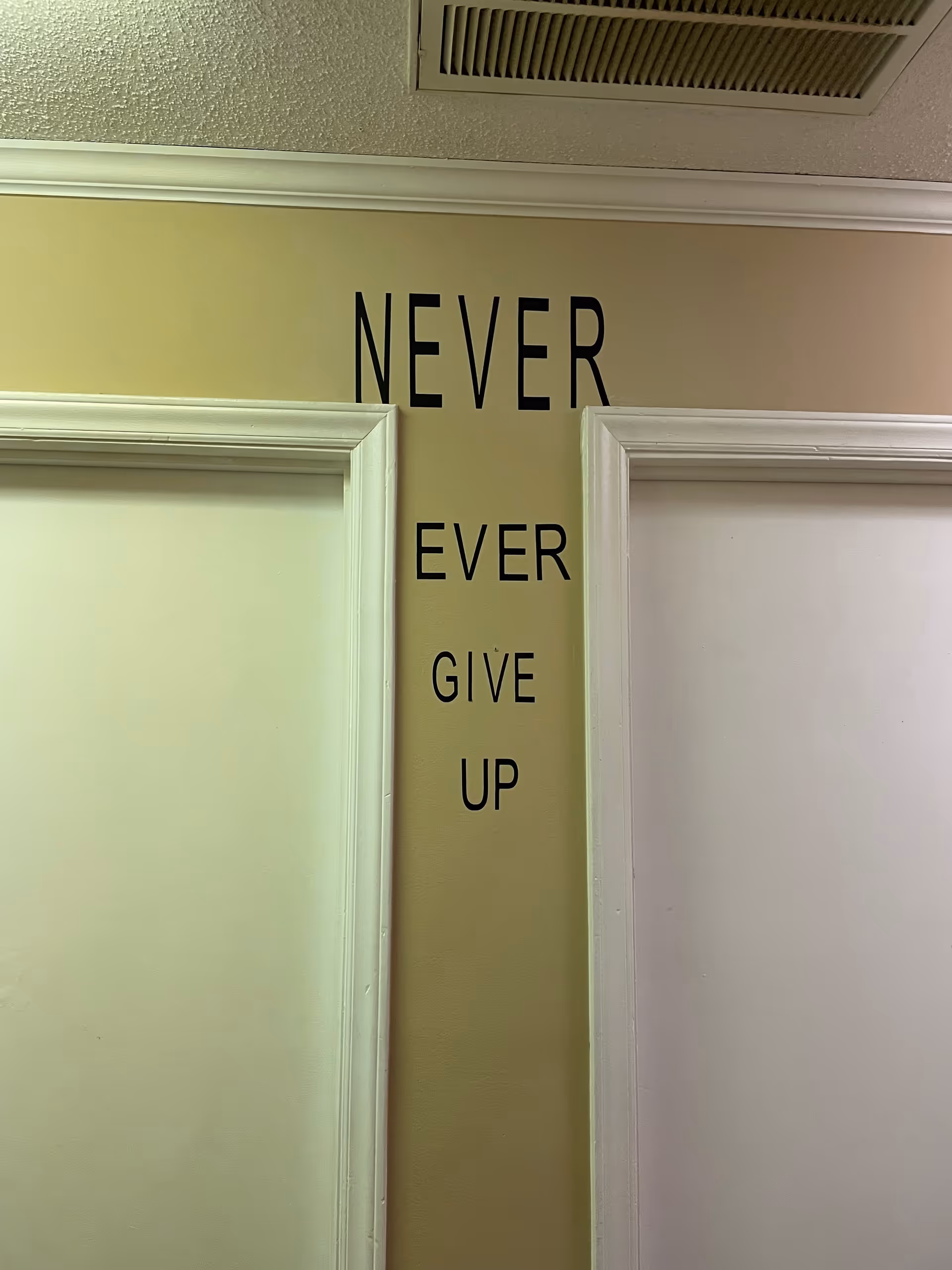 Interior hallway with beige wall and vertical black text reading NEVER EVER GIVE UP.