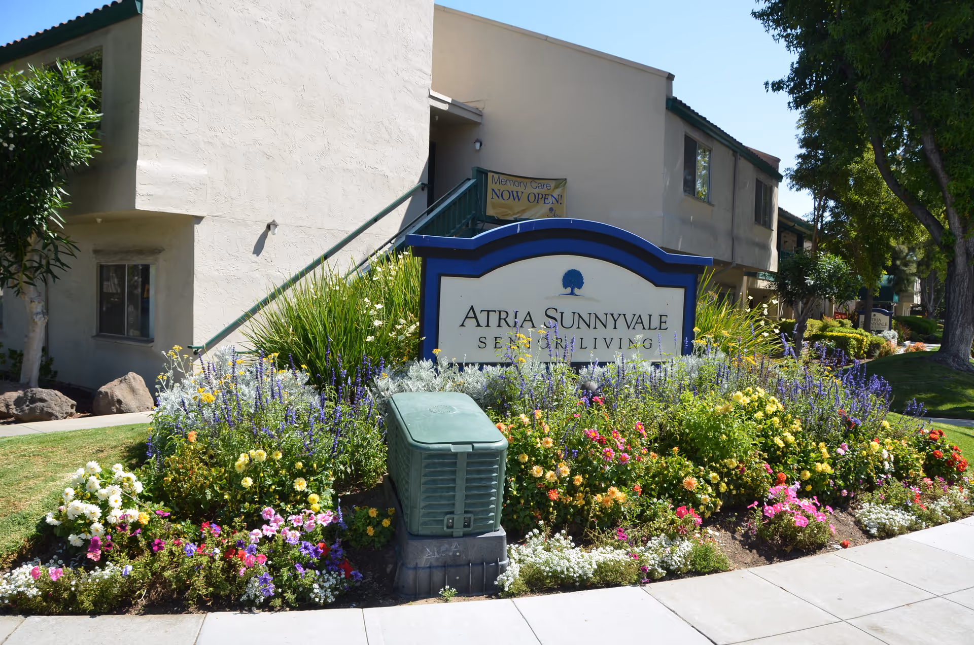 Exterior view of Atria Sunnyvale Senior Living with a colorful flower bed and sign