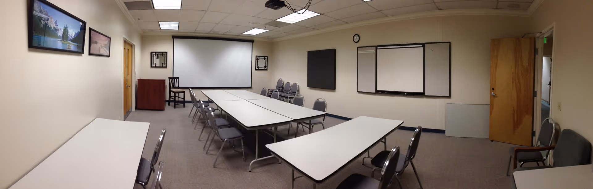 Interior meeting room in a senior facility with tables, chairs, whiteboards, and a projector screen.