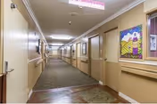 Narrow interior hallway inside a senior living center with doors and wall art.