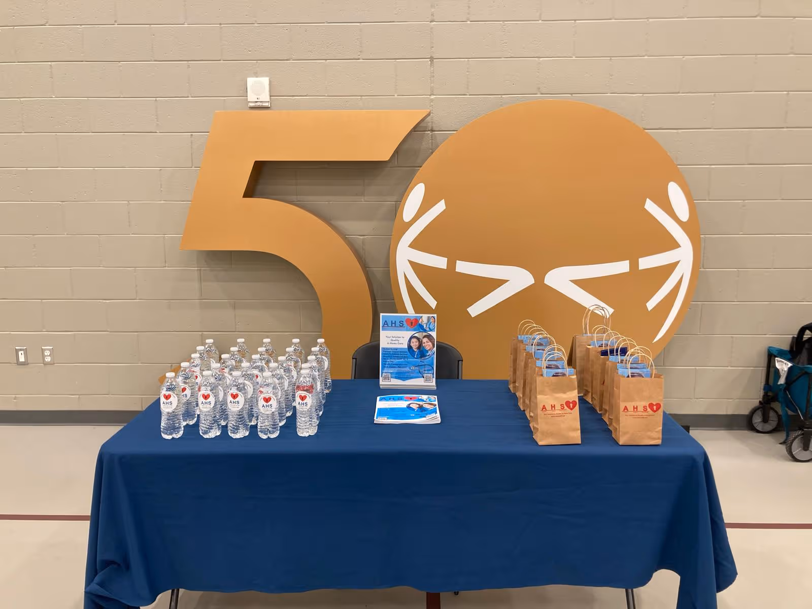 Event table with water bottles, paper bags, brochures, and an orange symbol.