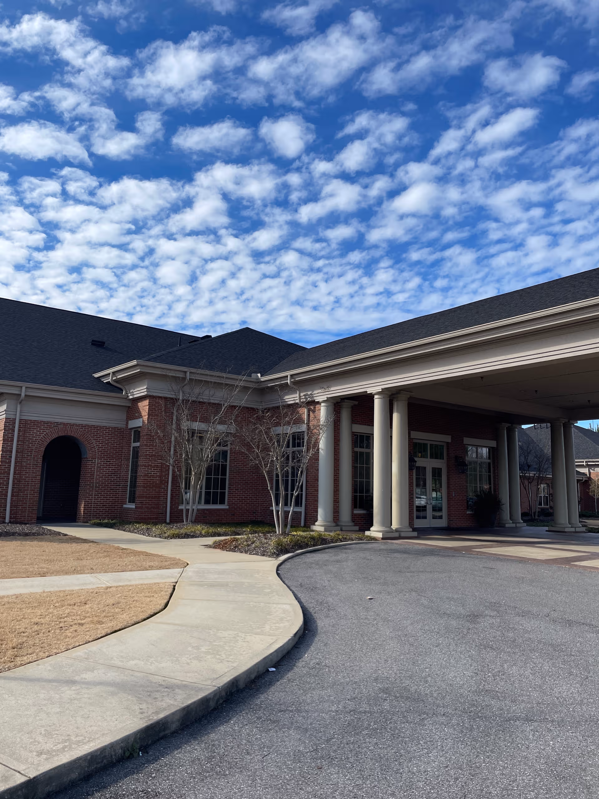 Brick senior living facility exterior with a covered entrance and curved driveway under blue sky.