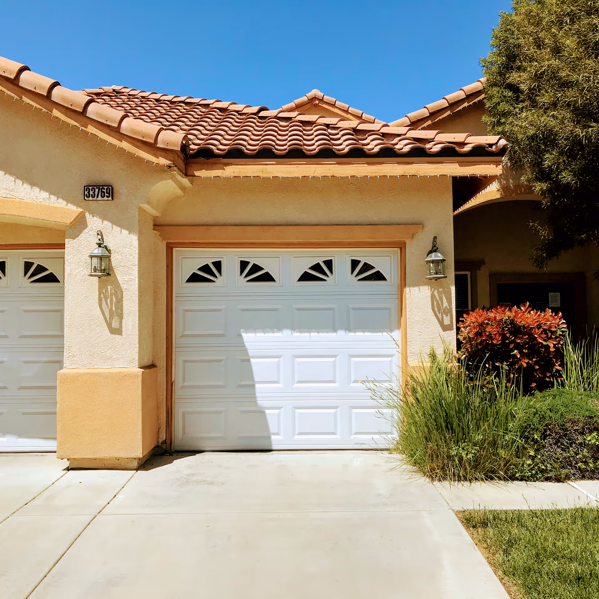 Cream stucco building with terracotta tile roof and white double garage door, landscaped right.
