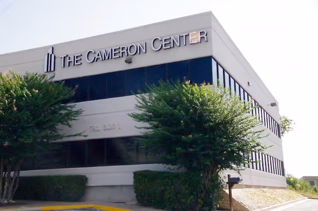 Exterior view of a gray building with 'The Cameron Center' sign and surrounding trees.