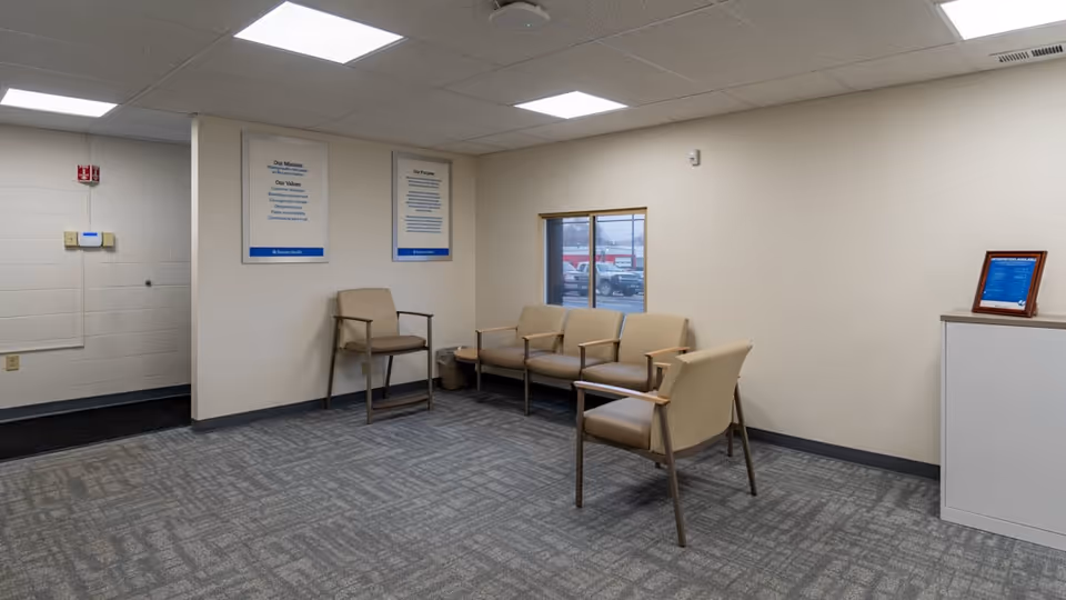 A spacious indoor waiting area with beige chairs and posters on the walls.