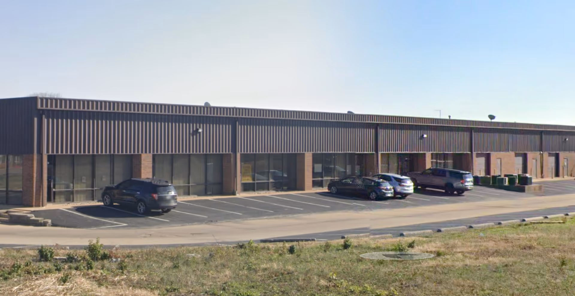 Exterior of a single-story facility with brick columns and parked cars in front.