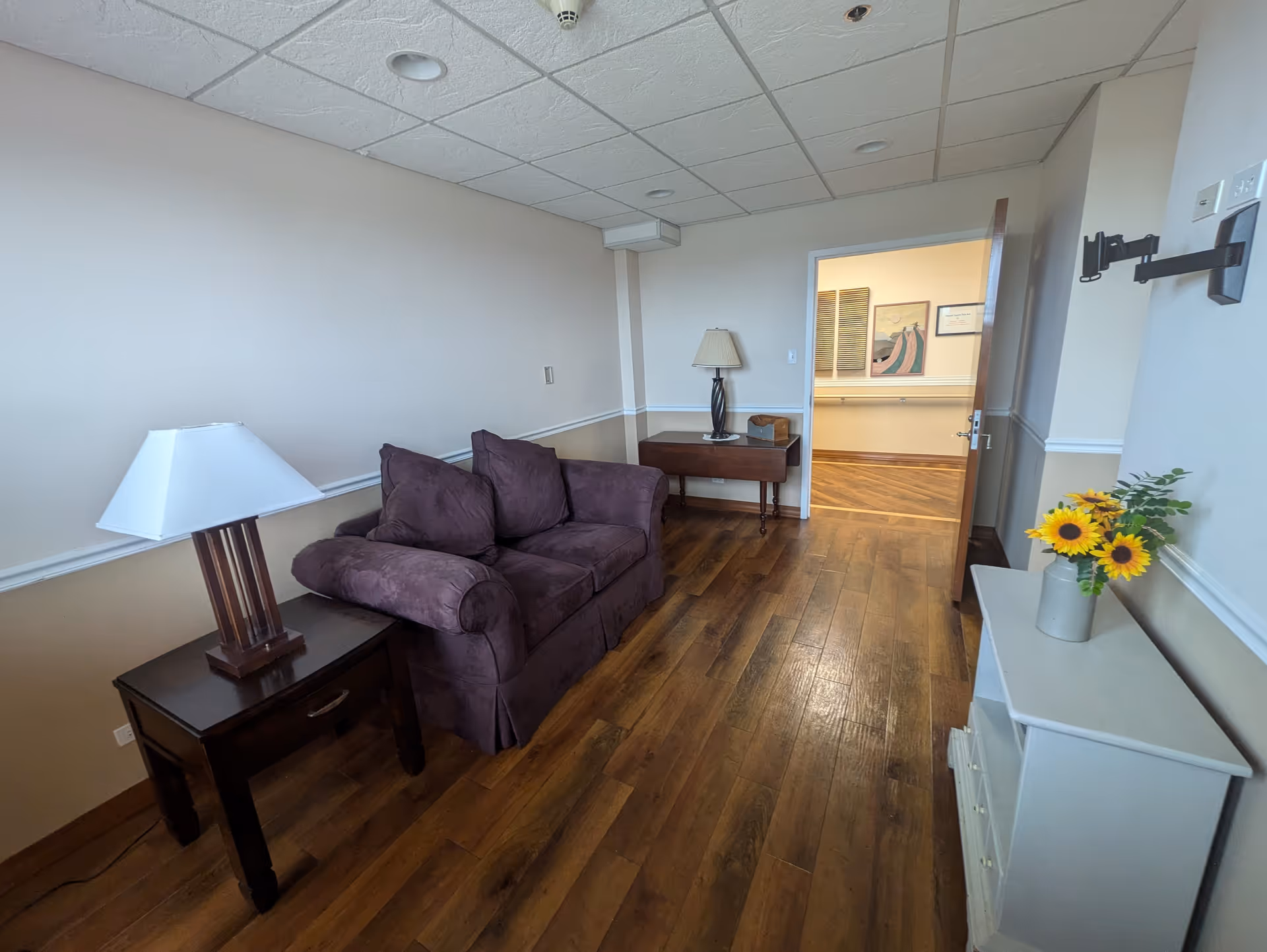Cozy living room in a senior facility with purple sofa, lamps, and sunflowers.