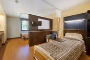 A furnished senior living bedroom with a bed, divider, and wood flooring.