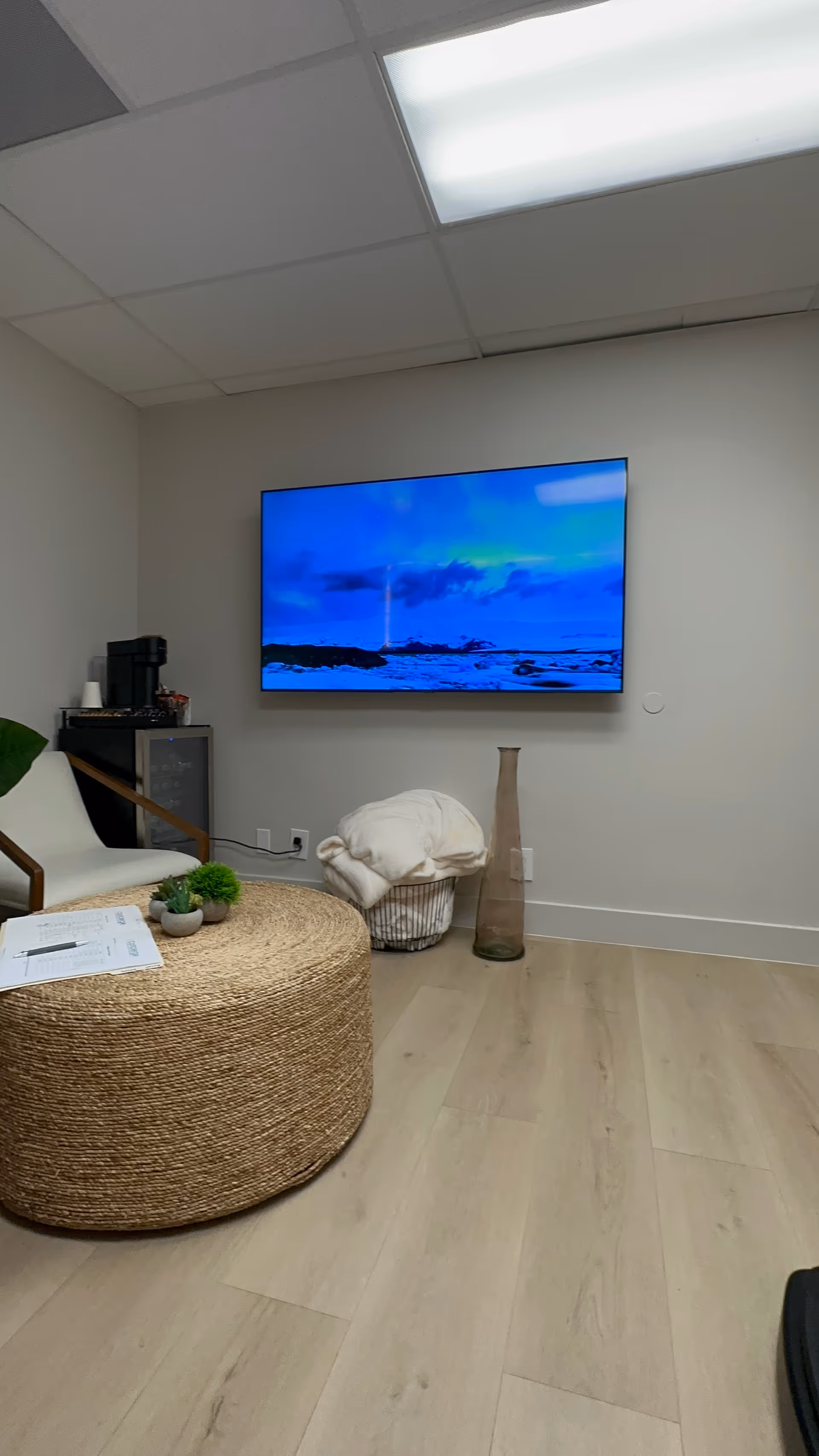 Cozy senior living facility lounge with wall TV, round wicker coffee table, and decorative accents.