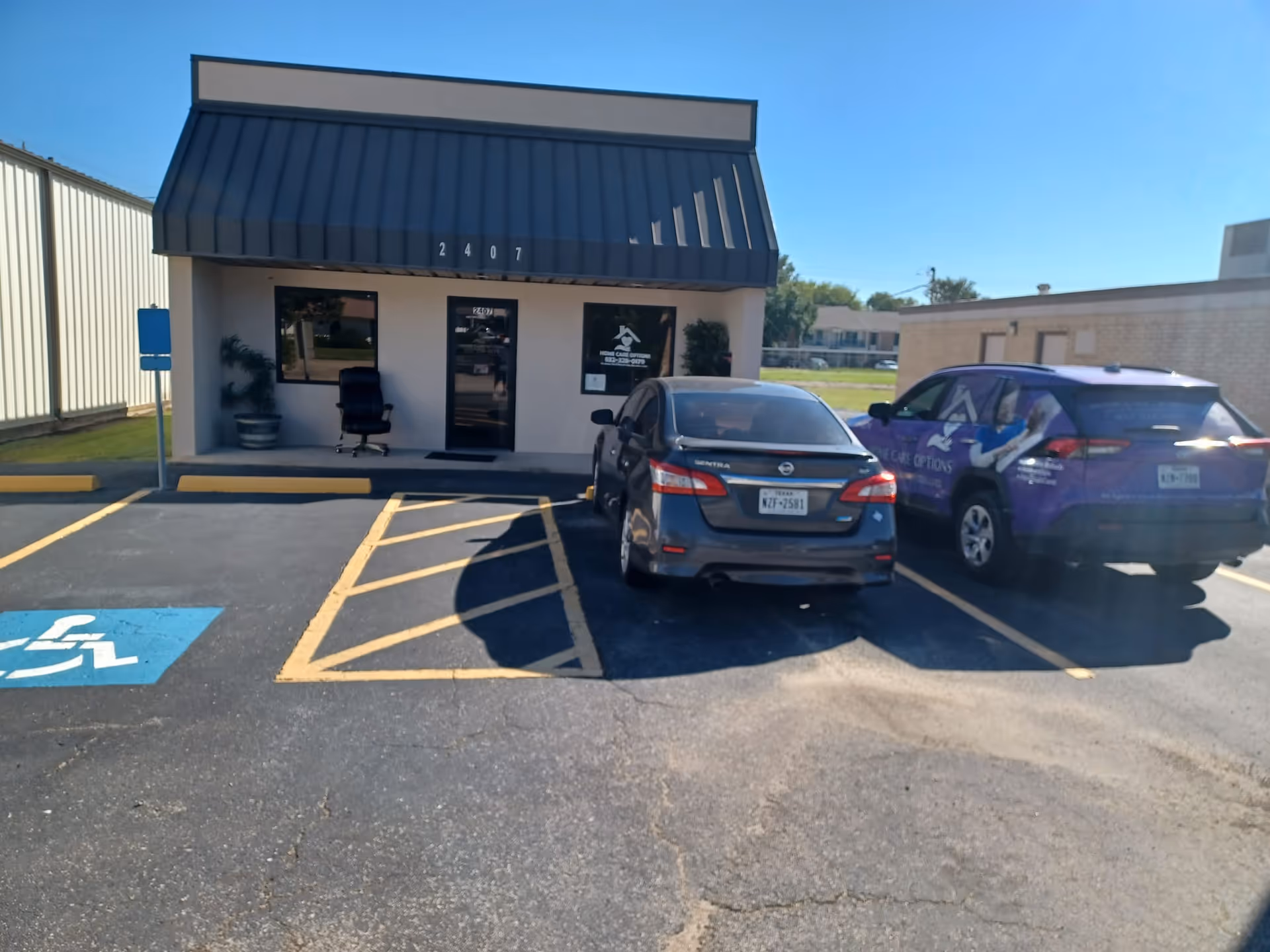 Small building with blue awning, two parked cars, and a wheelchair-accessible parking space.