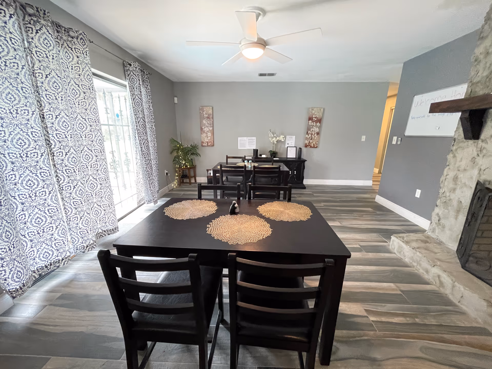 Dining room with dark wood tables and chairs, patterned curtains, and a stone fireplace.