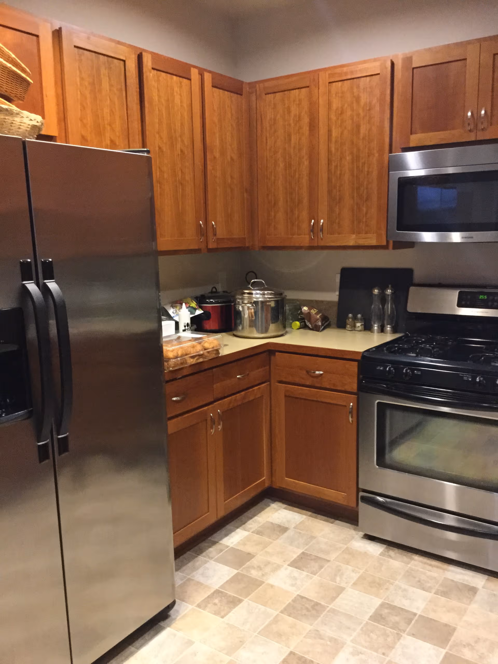 A kitchen with wooden cabinets, stainless steel appliances, and a beige tiled floor.