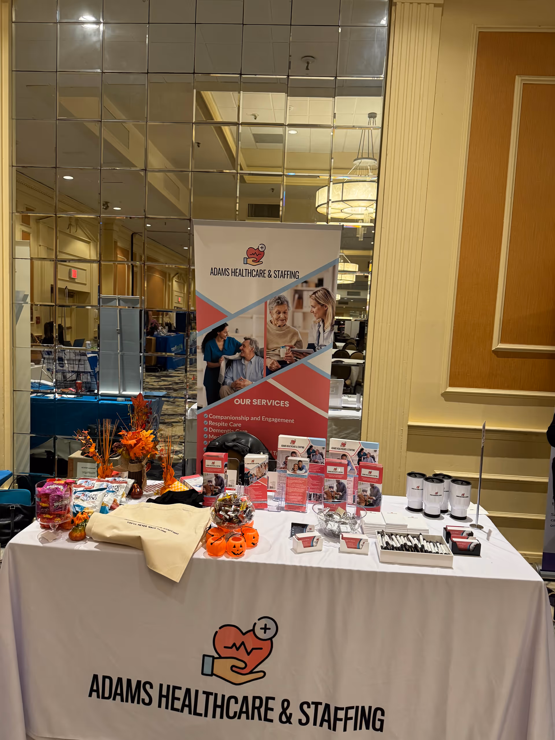 Indoor conference hall booth for Adams Healthcare & Staffing with banner and display table.