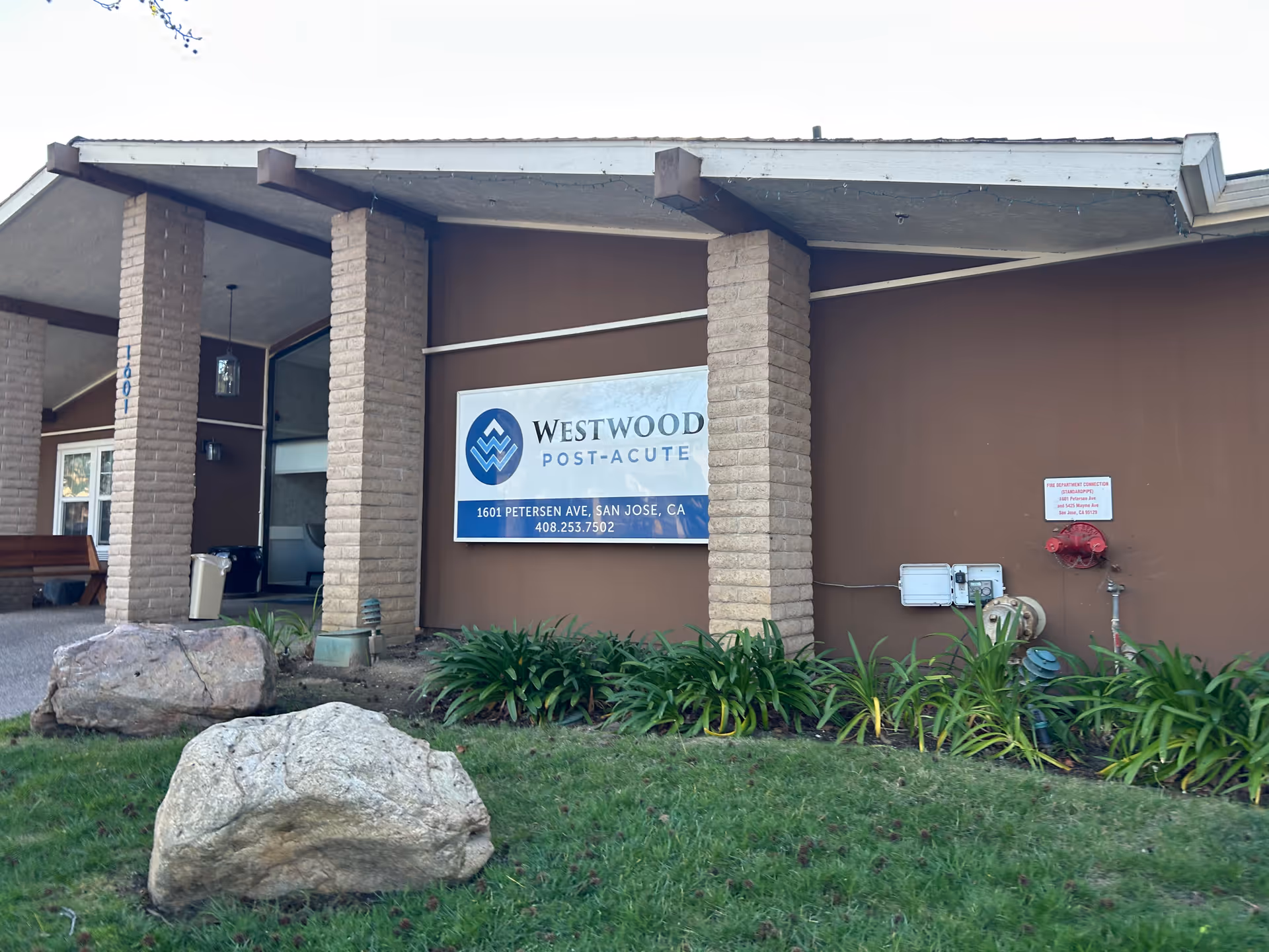 Front view of Westwood Post-Acute facility with sign, brown facade, and landscaped plants.