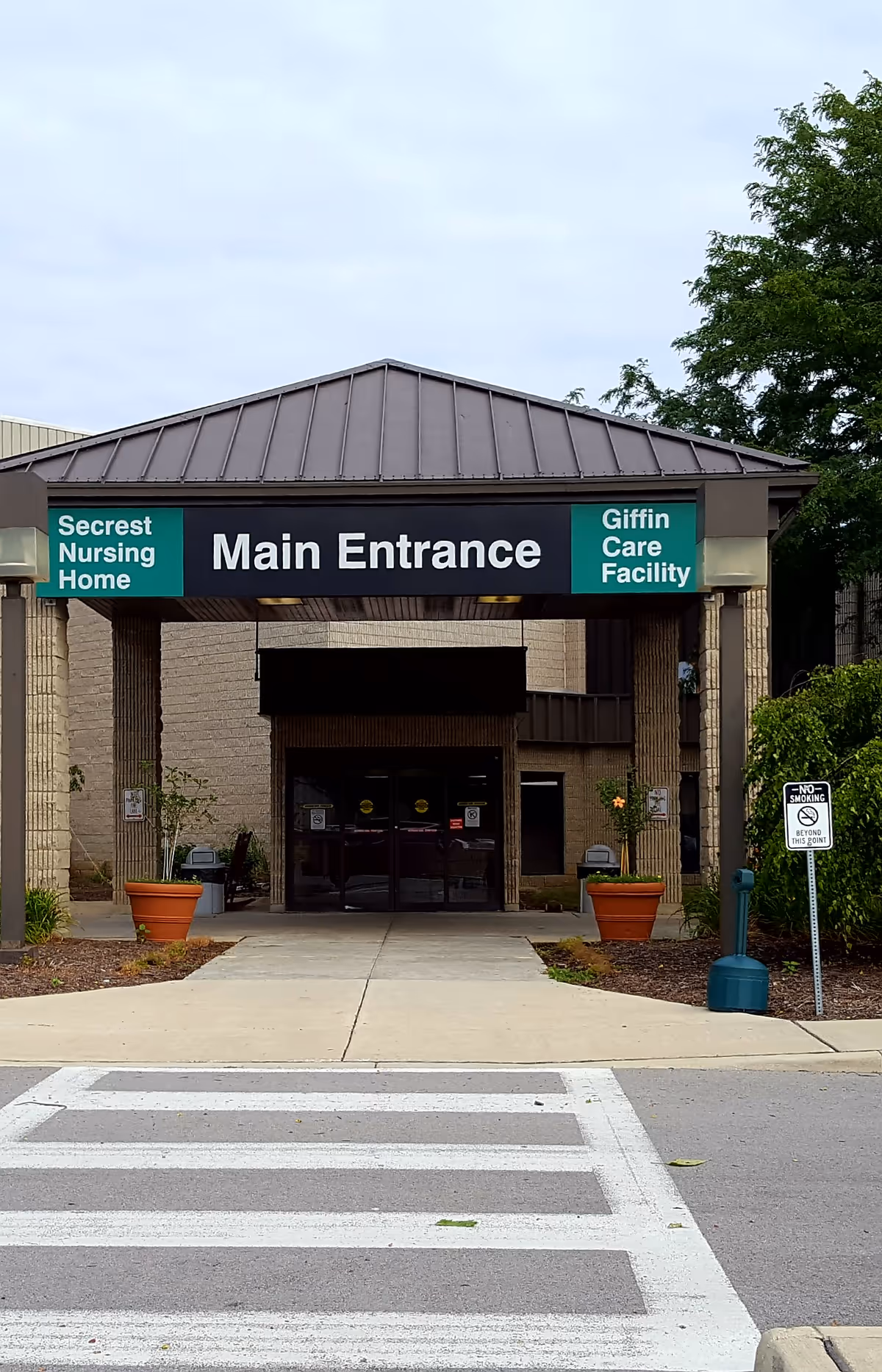 Exterior view of a nursing home entrance with a Main Entrance sign and planters
