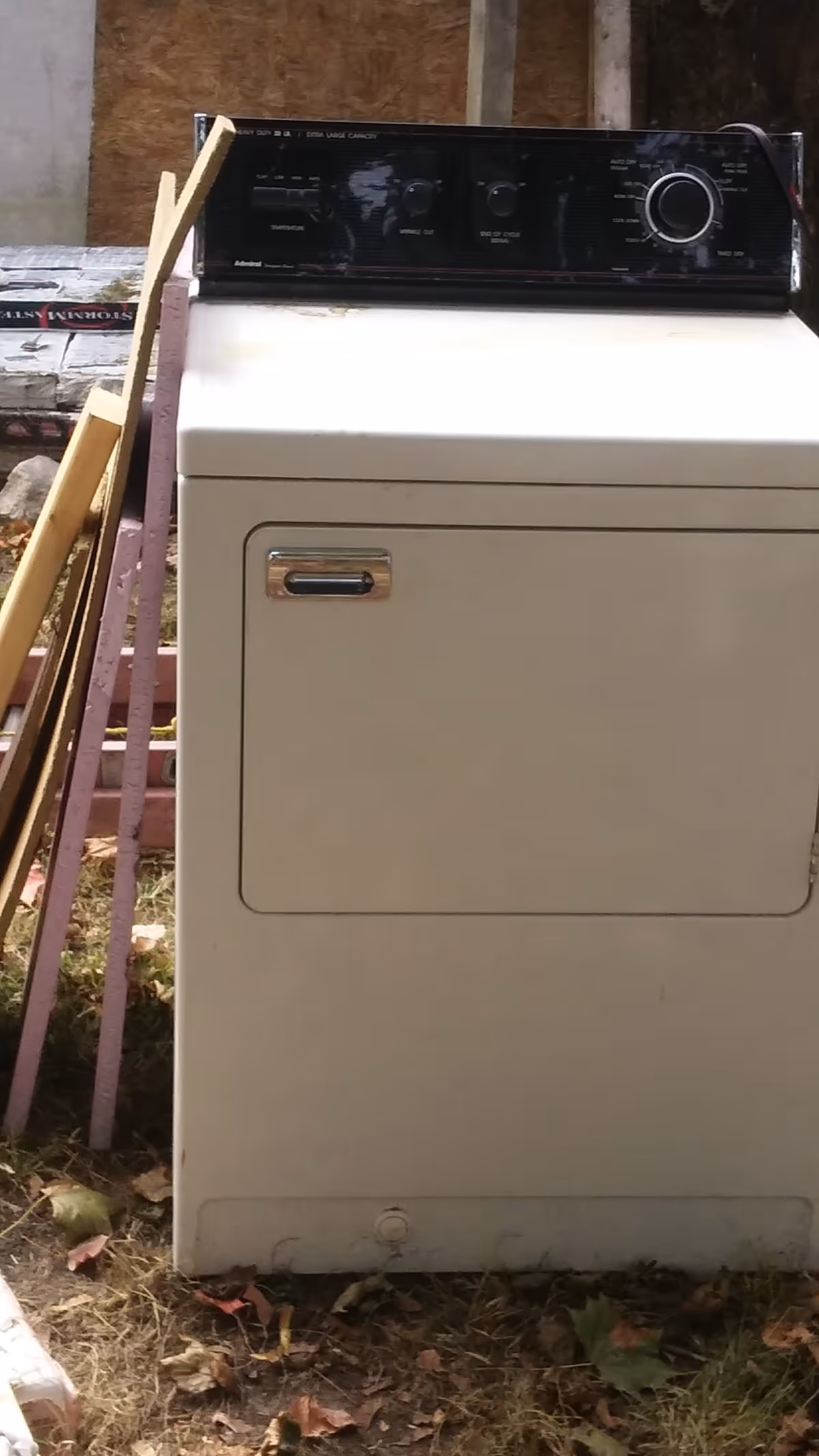 White top-loading washing machine outdoors beside railing and construction materials.