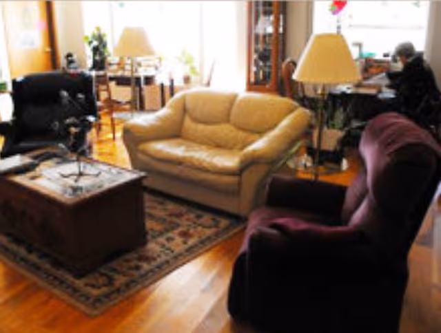 Living room with a beige loveseat, purple recliner, wooden coffee table on a rug, lamps and hardwood floors.