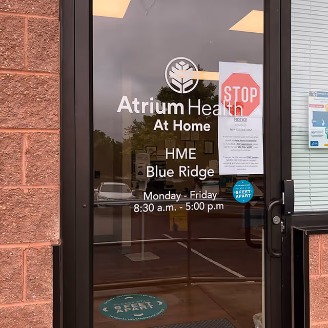 Glass door entrance displaying Atrium Health At Home signage and hours.