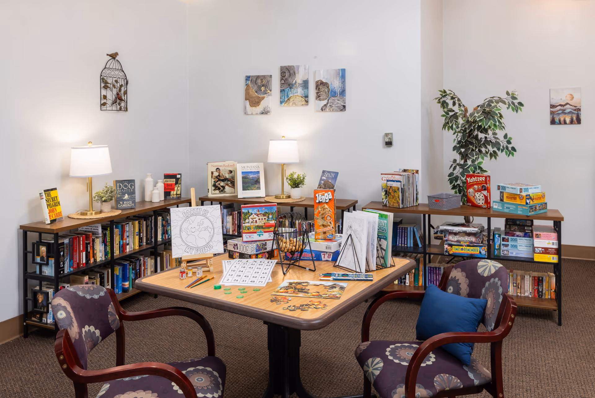 A bright senior living activity room with tables, bookshelves, games, and potted plant decor.