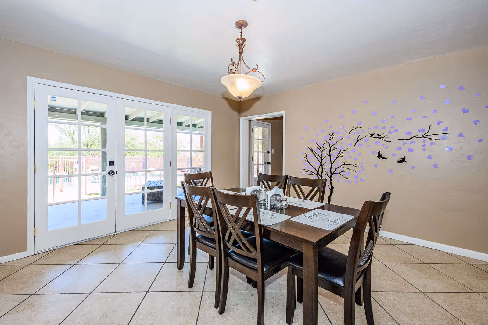 Dining room with a dark wood table, chairs, French doors, and a wall tree mural.