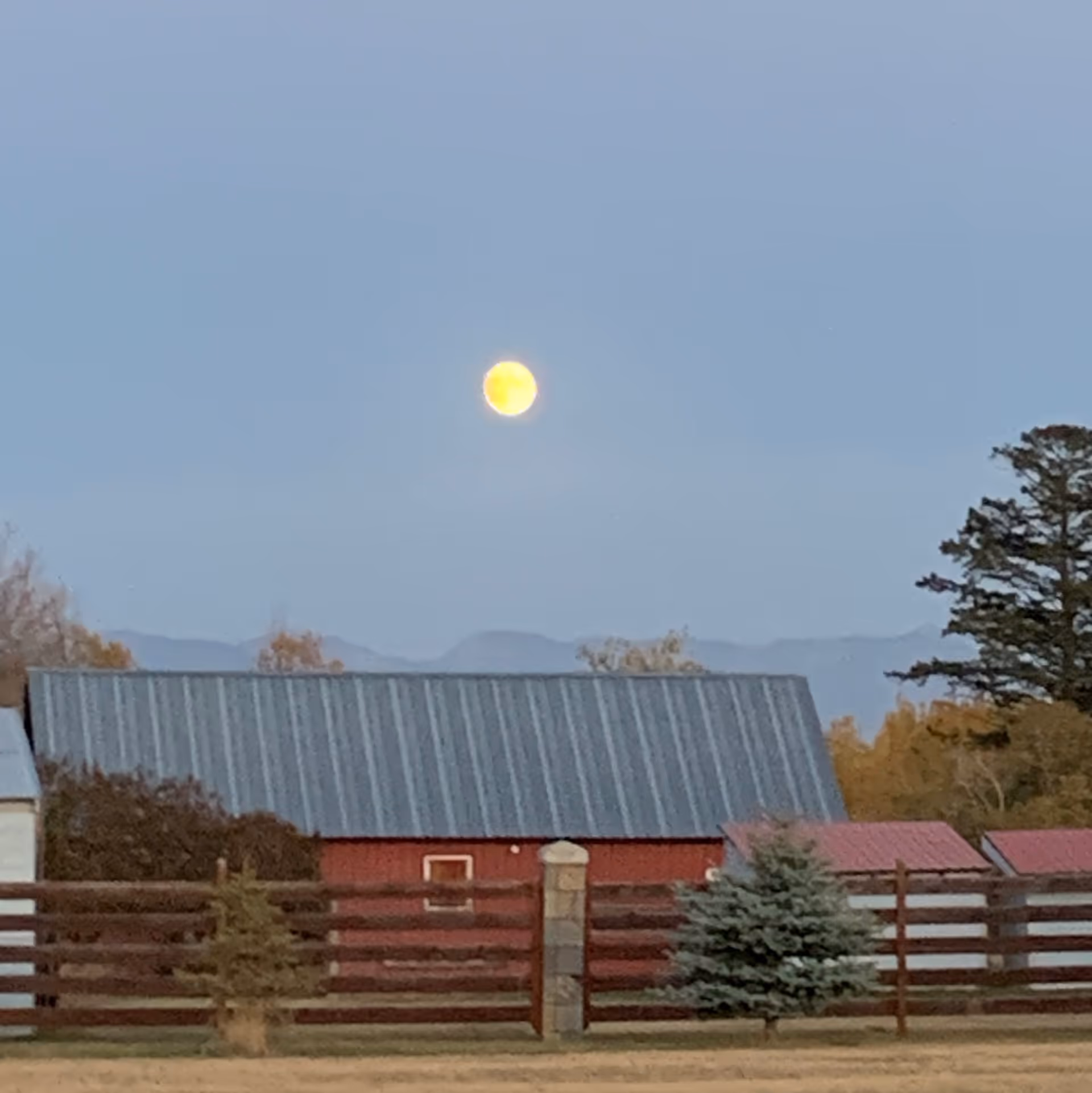 Moon over a rural property with a metal-roofed building and wooden fence.
