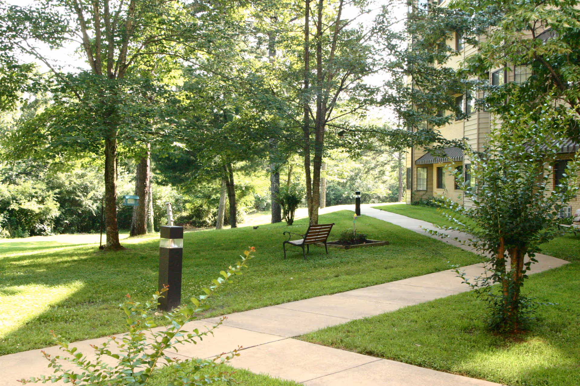 A landscaped outdoor courtyard with benches, a walkway, trees, and a building entrance.